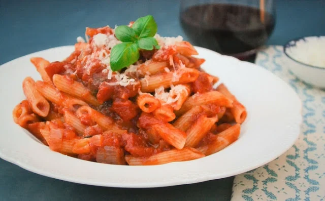 A white bowl of penne pasta in a basil and tomato sauce