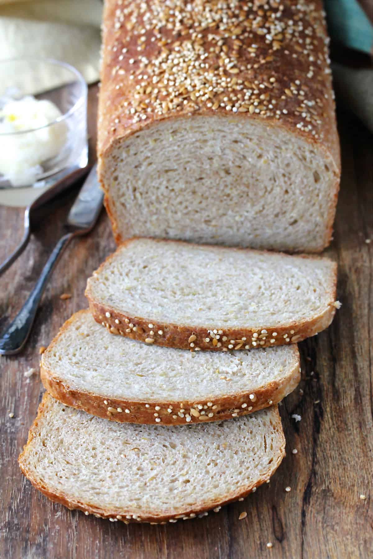 Whole Wheat Quinoa Bread sliced with a butter dish in the background.