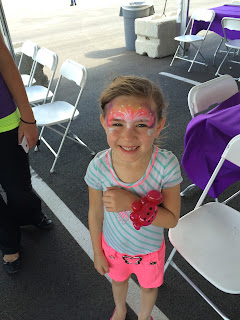 A little girl with her face painted and a balloon lady bug bracelet 