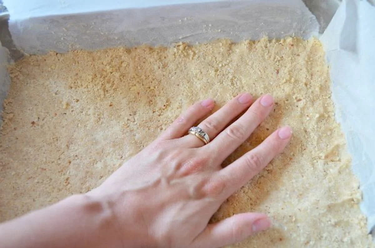 Shortbread Almond Crust being pushed into 9x13" baking pan lined with parchment paper.