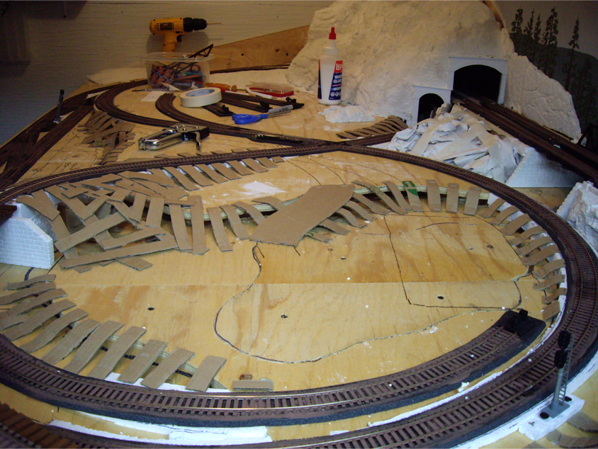 Cardboard strips being installed to the sides of a track grades and benchwork to form the base for hard shell terrain