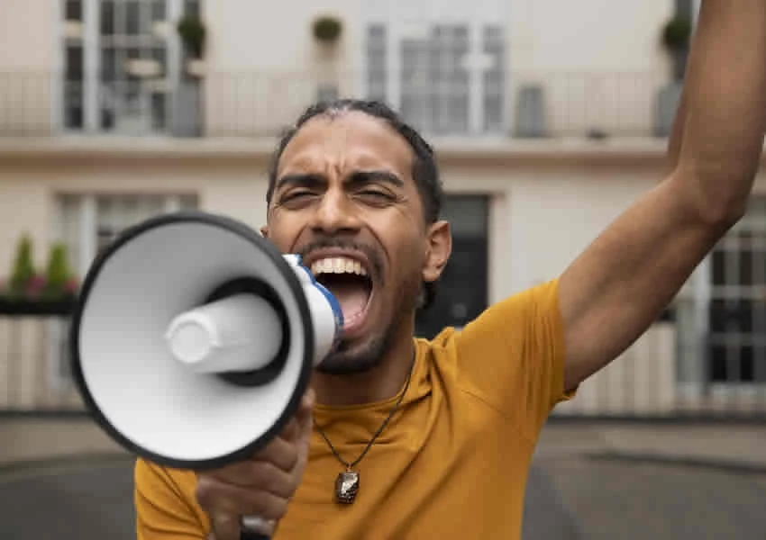 Imagem mostra um grevista gritando palavras de ordem em um megafone.