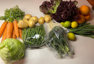 A collection of fruits and vegetables. Carrots, potatoes, green beans, broccoli, cabbage, lettuce, limes, oranges, green onions.