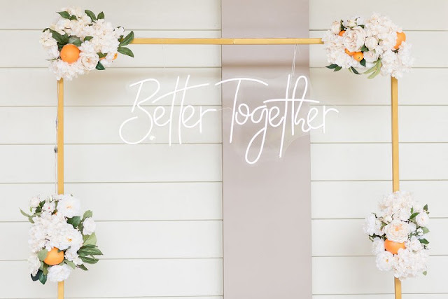 better together neon sign from at last weddings hung on copper stand with white bouquets and oranges