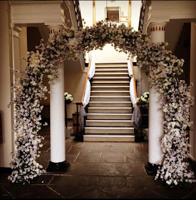 white floral arch at bottom of staircase at wedding venue 
