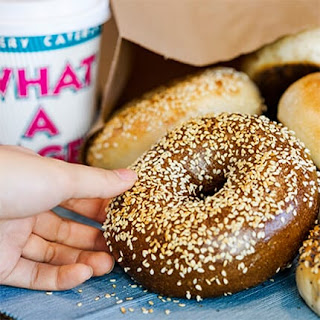 Handing reaching for a a bagel with a cup that says What a bagel behind it.