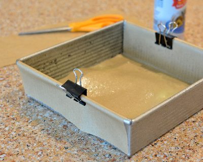 A baking pan prepped with a parchment sling held in place by metal binder clips.