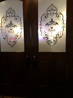 a set of double wooden doors with the upper half in frosted fleur decorated glass