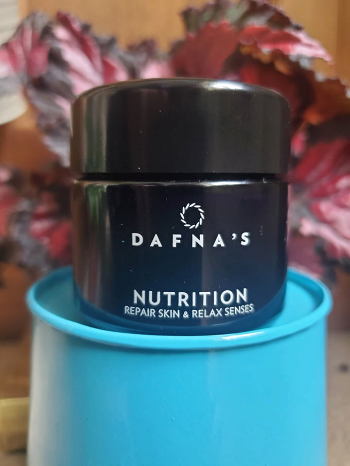 Dafna's Skincare Nutrition Moisturiser on a light blue stand with leafy red and black begonia behind