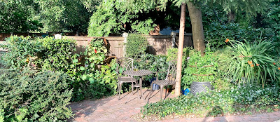 Picture of a garden patio, table, two chairs, surrounded by shrubs and flowers