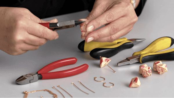hands holding pliers while making patterned paper origami jewelry
