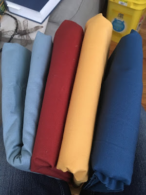 Four folded pieces of broadcloth: a grey-blue, an orangey red, a pale soft yellow, and a clear medium blue.