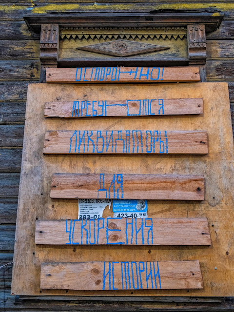 Надпись на стене деревянного дома "Осторожно! Требуются ликвидаторы для ускорения истории"