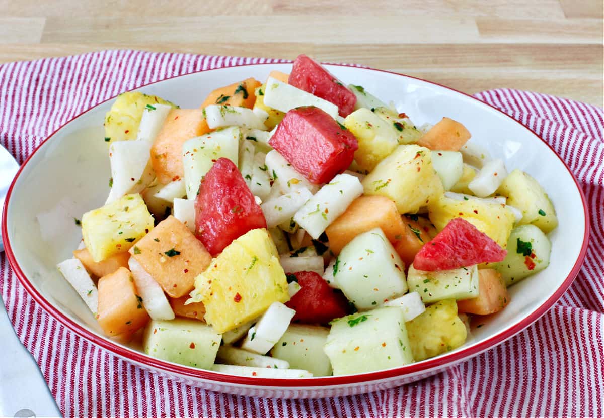 Melon, Jicama, and Pineapple Salad in a white red rimmed bowl.