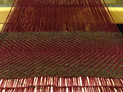 A close-up of the first repeat of a diagonal twill in brown on maroon, which makes a chevron pattern very like a raw tuna filet.