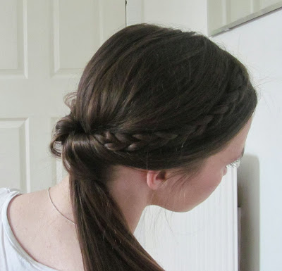 Back of woman's head with brown hair with small plait down side pulled inside bobble at nape of neck into low ponytail