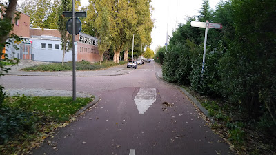 Une piste cyclable rouge à double sens rejoint une rue résidentielle avec un tracé similaire à la photographie précédente.