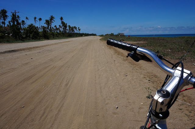 Bicycle handlebar at the foreground with a long dusty road in the background