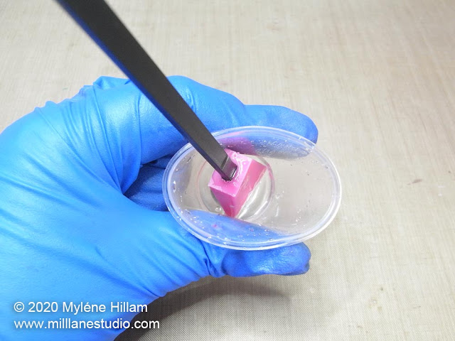 Gloved hand holding a plastic cup with a silicone stirrer standing up in cured resin