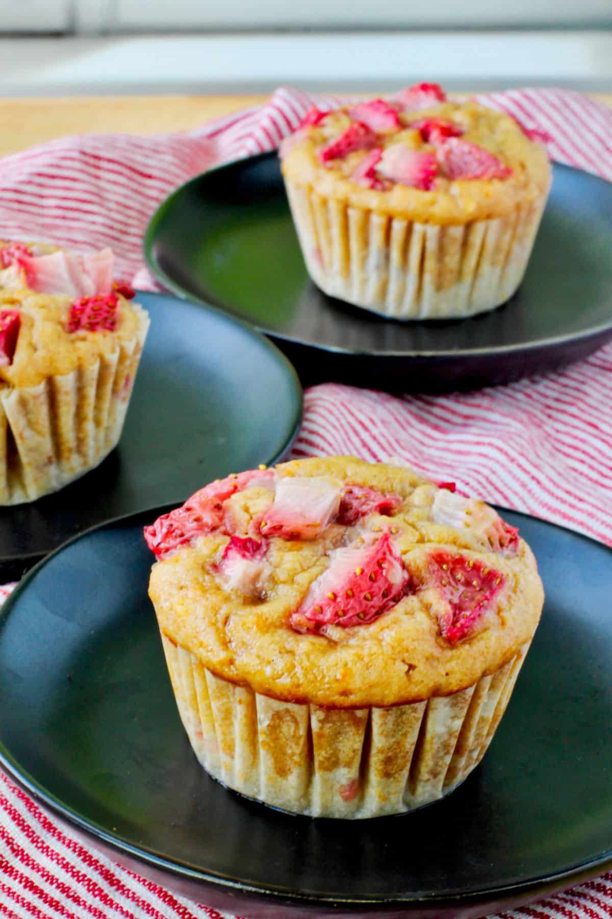 Orange and Strawberry Whole Wheat Muffins on black plates.