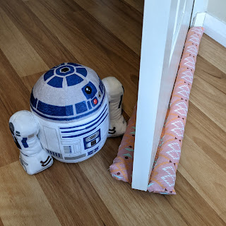 An ajar door with double snake on either side of the base, beside a plushie R2D2 door stop.