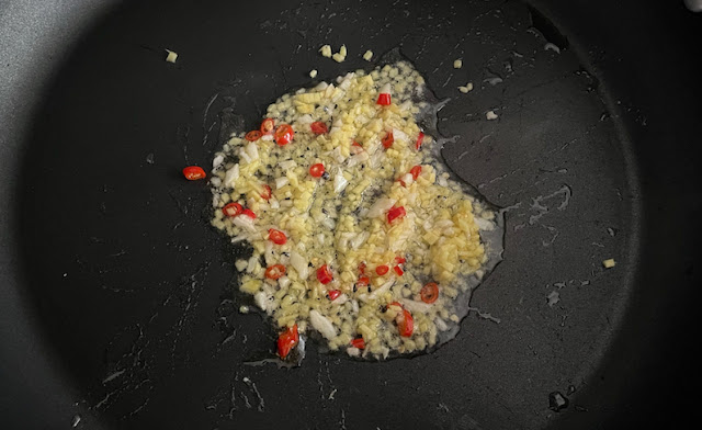 A frying pan with oil and minced ginger and garlic and sliced red chili peppers.