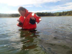 Pelastautumispukuinen henkilö seisoo vyötäröä myöten vedessä ja ihmettelee jotain kädessään