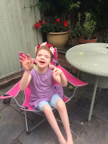 picture of daisy in a pink garden chair smiling and waving at the camera