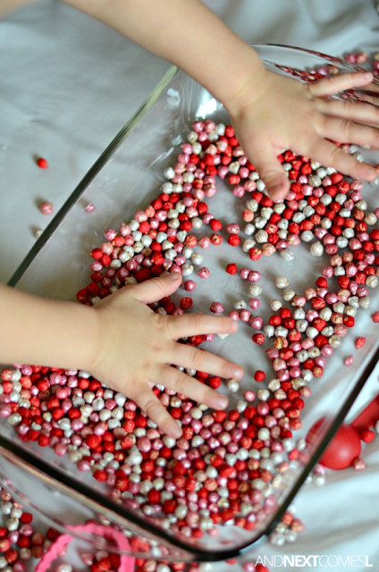 Close up of child's hands playing with red, pink, and white dyed chickpeas