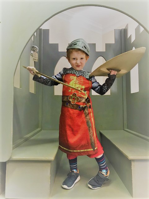 Little boy dressed as a knight holding a sword and shield and pulling a face