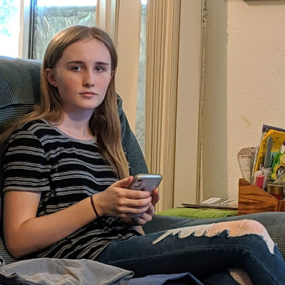 Teenage girl sitting with phone wearing ripped jeans and striped tshirt