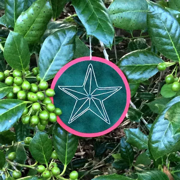 embroidered paper star ornament hanging on holly bush with green berries