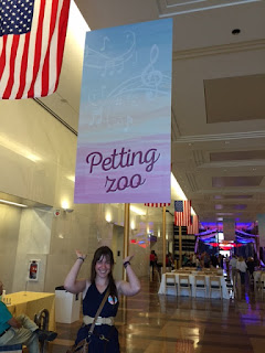 Photograph of me standing below a pink, yellow, and blue banner that reads "Petting Zoo"