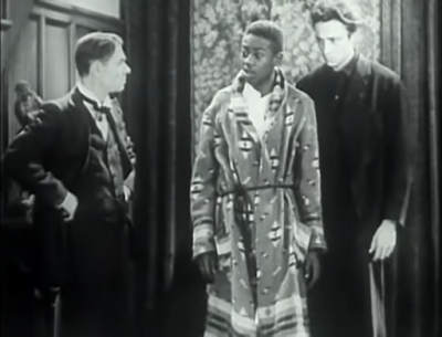 Actor Willie Best wears a dressing gown and stands between two-well-dressed men