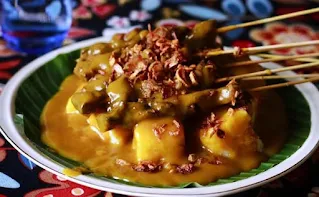 Tusukan sate daging khas Minang yang matang sempurna dengan bumbu kacang khas, disajikan di piring dengan taburan bawang goreng dan irisan cabai merah.
