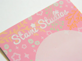 A photo showing the presentation card for a pin badge by the company Stami Studios. It is pink decorated with stars and plants in different colours