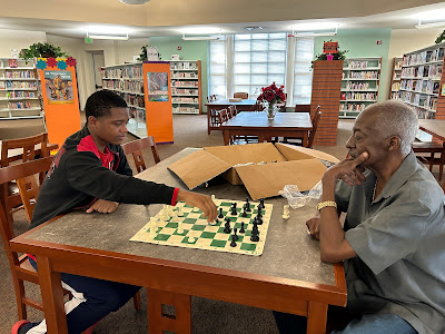 A young student plays against the older teacher in a chess game.