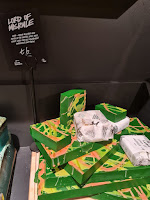 A photo of a light brown rectangular shelf filled with green and black square pieces of soap with a ornate white design on the front of each slice next to a black rectangular card that says Lord of Misrule soap in white font on a bright background