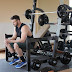 Man in black tank top and blue nike shoes sitting on bench press