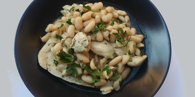 Chicken and white bean broth with parsley in black bowl