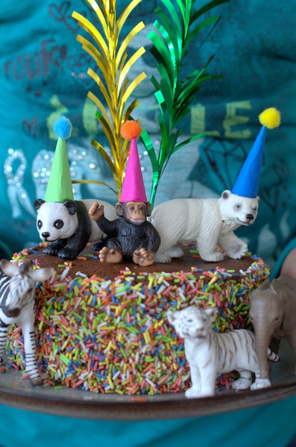 Bunter Partykuchen mit Streuseln und Tierfiguren, die lustige Partyhüte auf den Köpfen tragen.