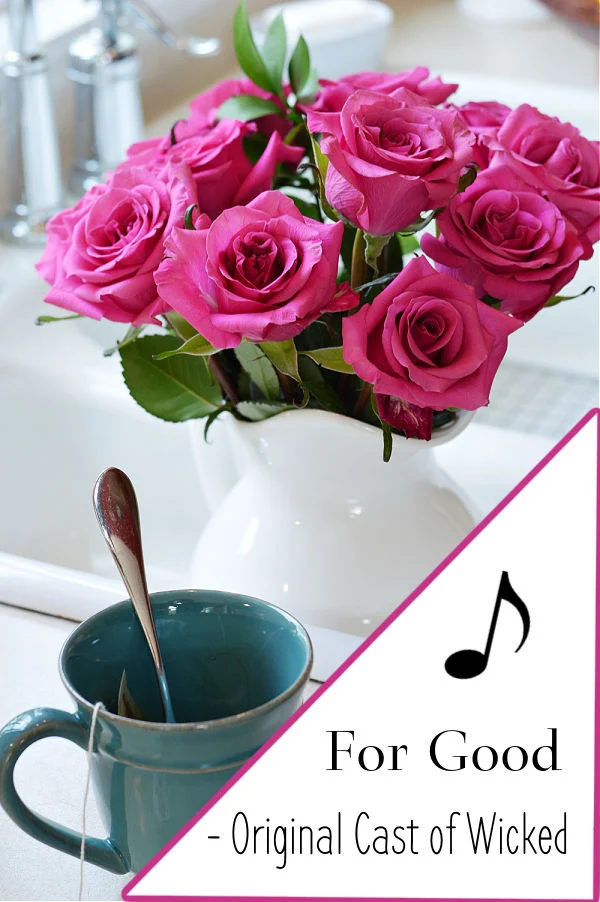 For Good By The Original Cast Of Wicked text next to a teal coffee cup and a vase of pink roses