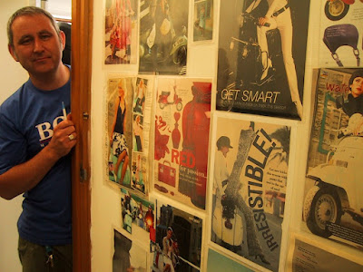 Man standing next to a wall covered with pages cut out of fashion magazines containing scooters