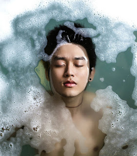 Visão superior de rapaz oriental deitado na banheira de olhos fechados e cabelos mergulhados na água com espuma de shampoo