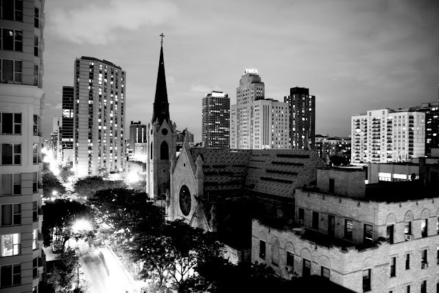 A very of buildings and a church in Chicago at night from an apartment balcony.