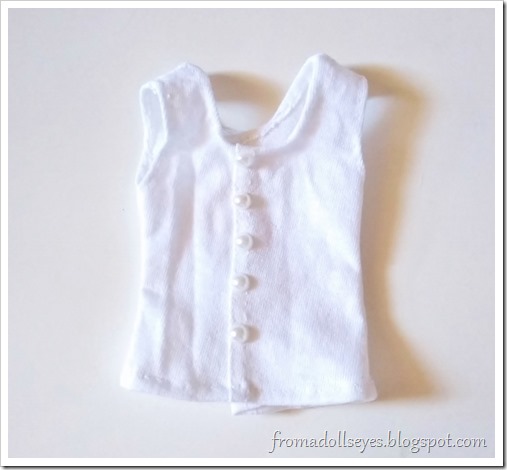 A white doll sized tank top with faux pearl "buttons" down the front.  The button front is fake, the top opens in back with velcro.