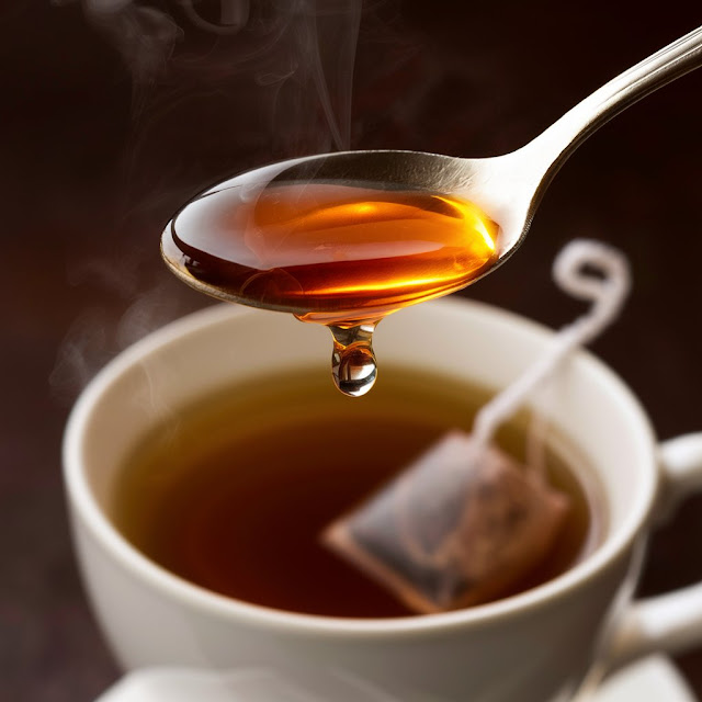 A close-up image of honey being drizzled over a spoon or a cup of tea.