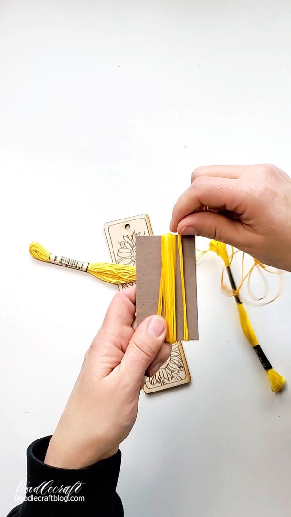 Use a 2.5 or 3" piece of cardboard to wrap the 3 strands of embroidery floss around.   Wrap the strings around the cardboard about 10-12 times.
