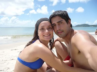 Pareja sonriendo y sentados en la arena con las caras muy juntas