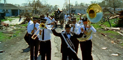 A New Orleans funeral procession marching a symbolic casket marked Katrina amidst the wreckage of Hurricane Katrina. It's lead by a brass band.